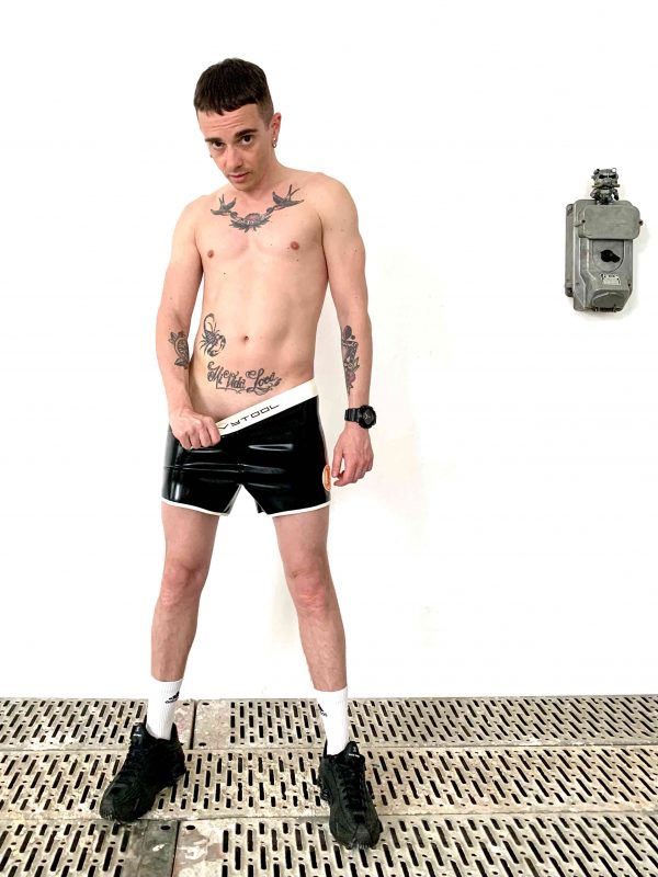 Rubber Latex Fetisch Hotpants. kurze Hose in schwarze, mit Seitenstreifen in weiß orange und weißem Bund mit Logoschrift. Für Jungs, Kerle und Männer, gay, queer